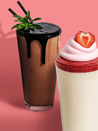 Two beverages are on a pink background. On the left is a chocolate shake with chocolate syrup dripping down the side and a sprig of mint on top. On the right is a layered dessert in a glass, with a white base, a red layer, pink whipped cream, and a strawberry on top.