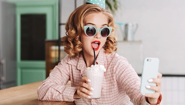 A woman holding a shake and taking a selfie