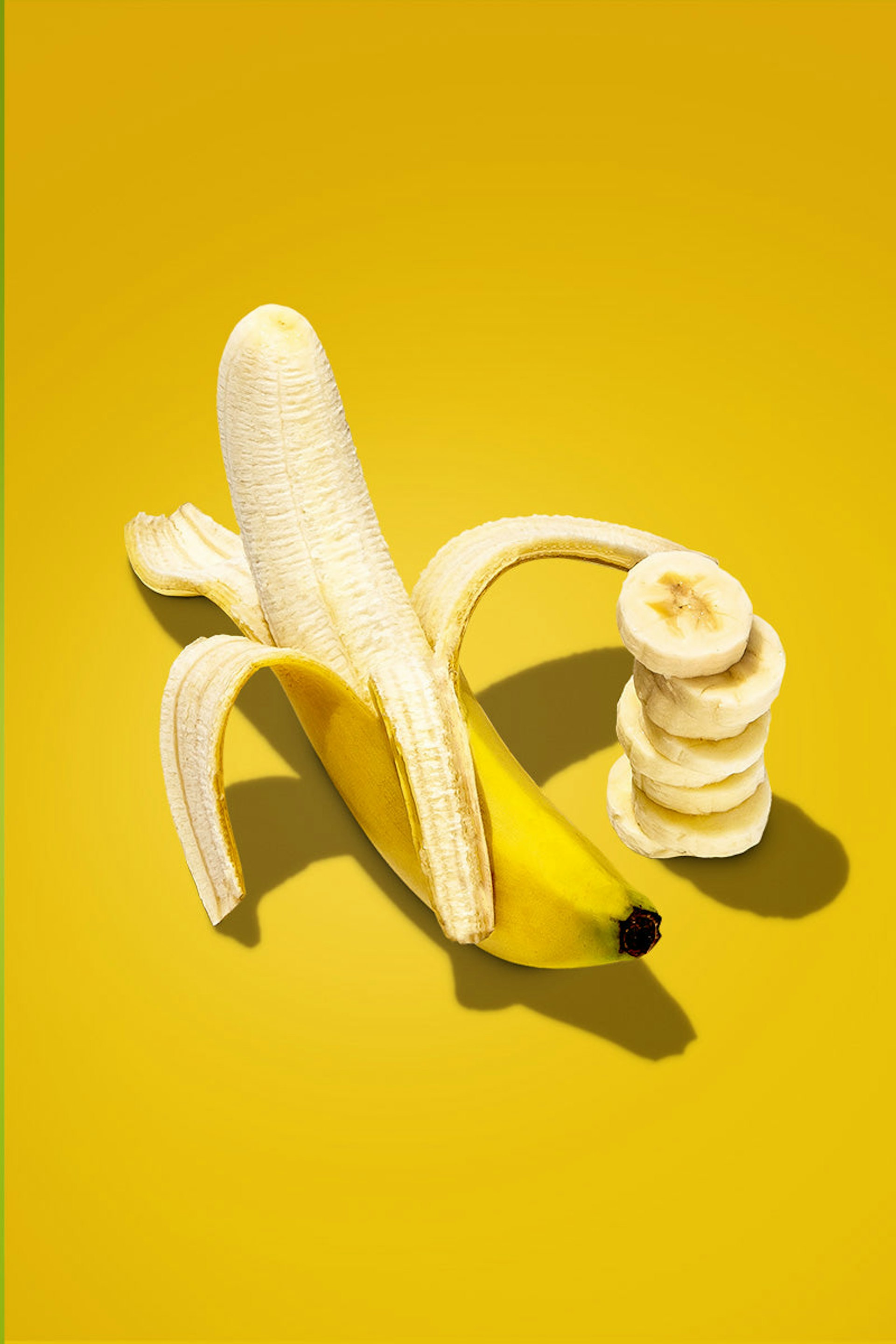 A partially peeled banana, with extra banana slices on the side