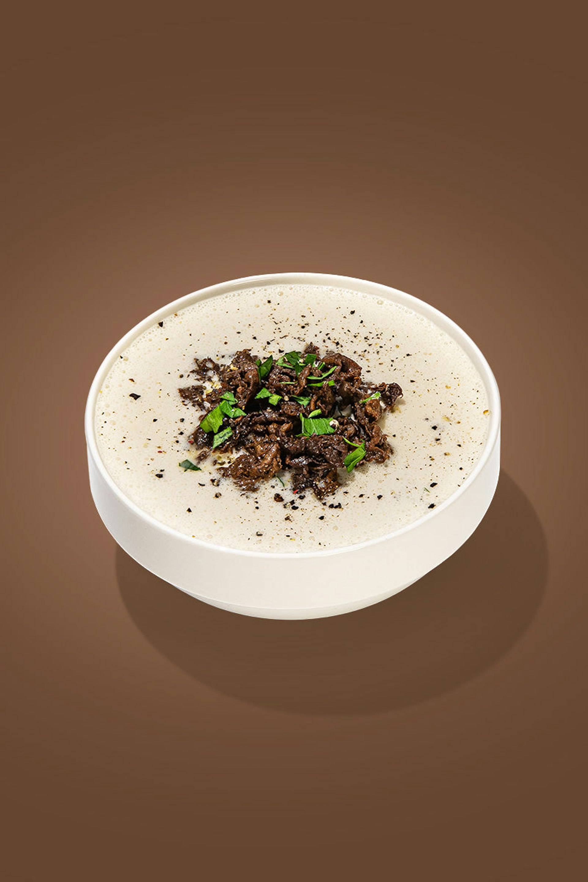 A bowl of beef broth, garnished with shredded beef and crushed black pepper