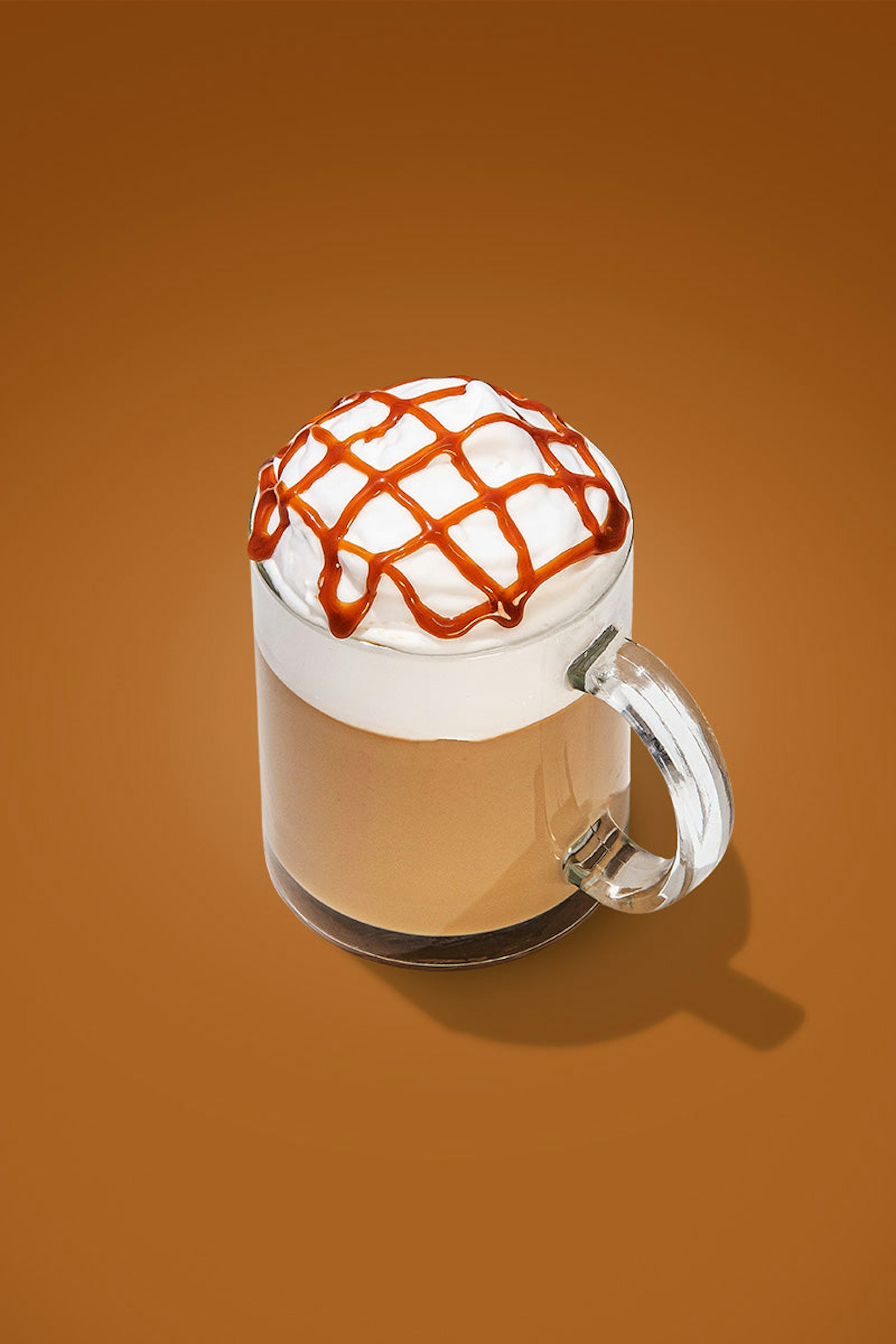 A caramel macchiato, topped with whipped cream, and caramel sauce drizzled on top in a lattice pattern