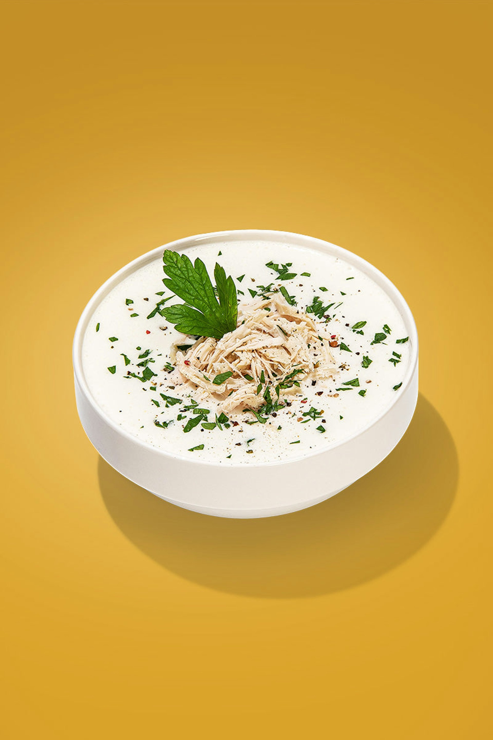 A bowl of creamy chicken soup, garnished with shredded chicken and parsley