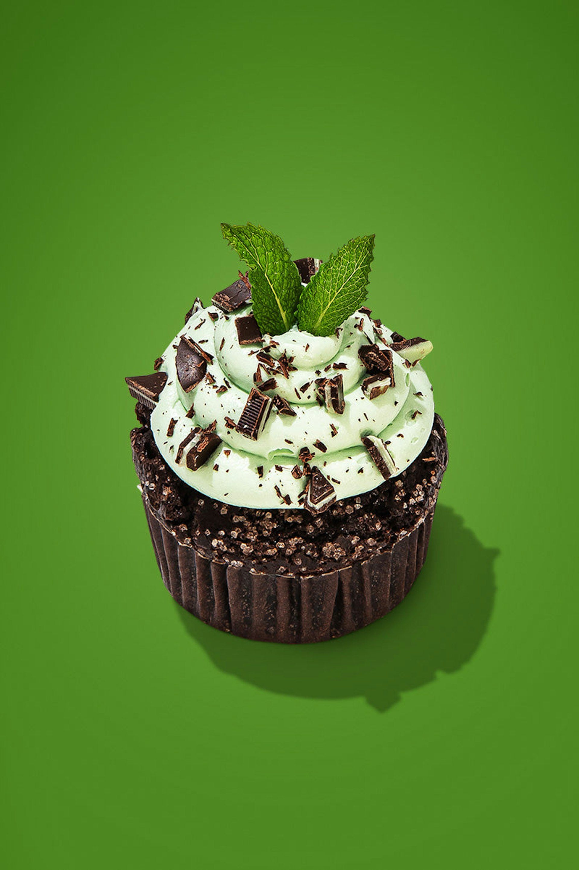 a chocolate mint cupcake with lots of minty frosting and garnished with chopped chocolate and a sprig of fresh mint