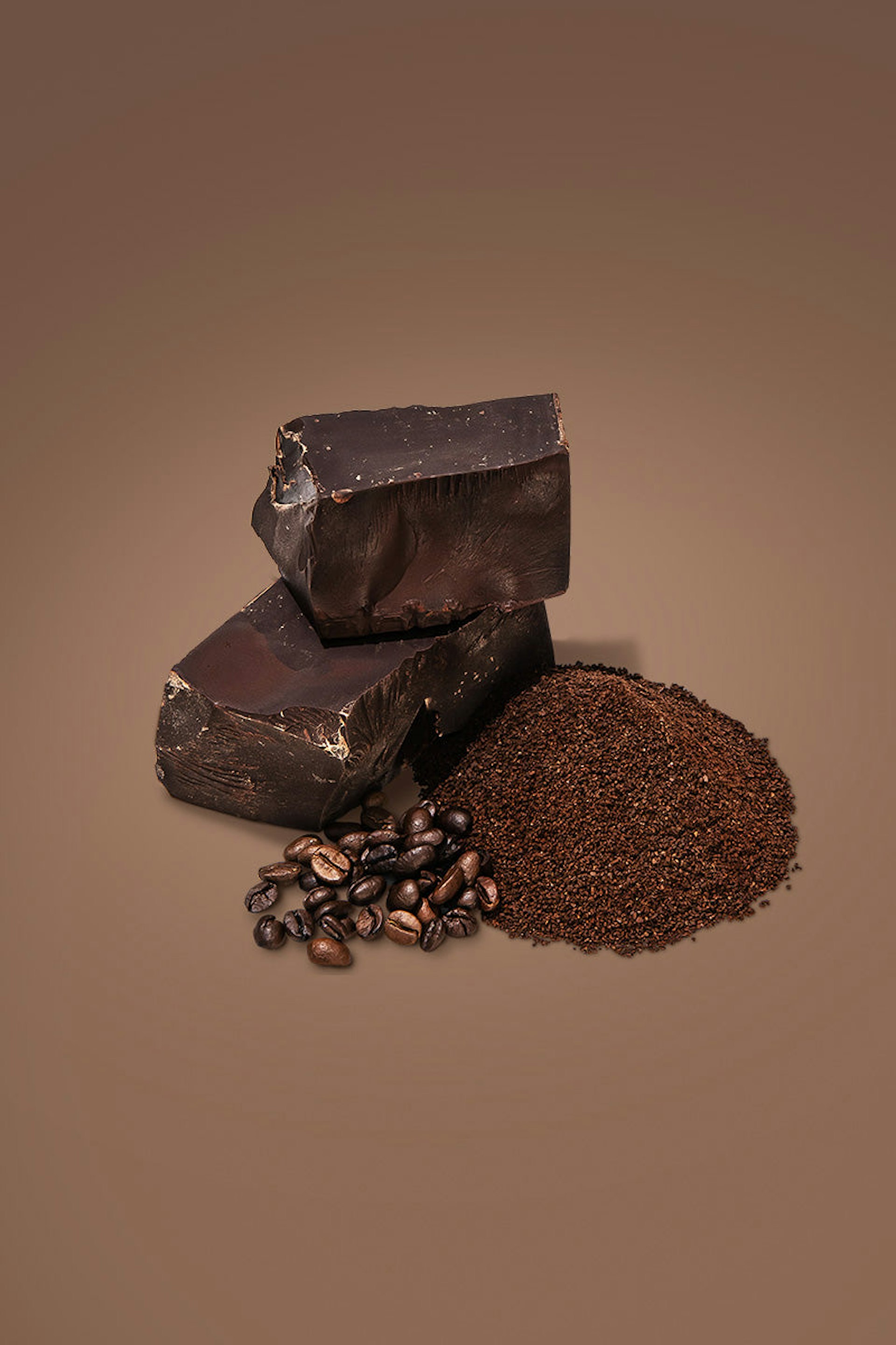 Two thick chocolate bars next to some coffee beans and ground coffee