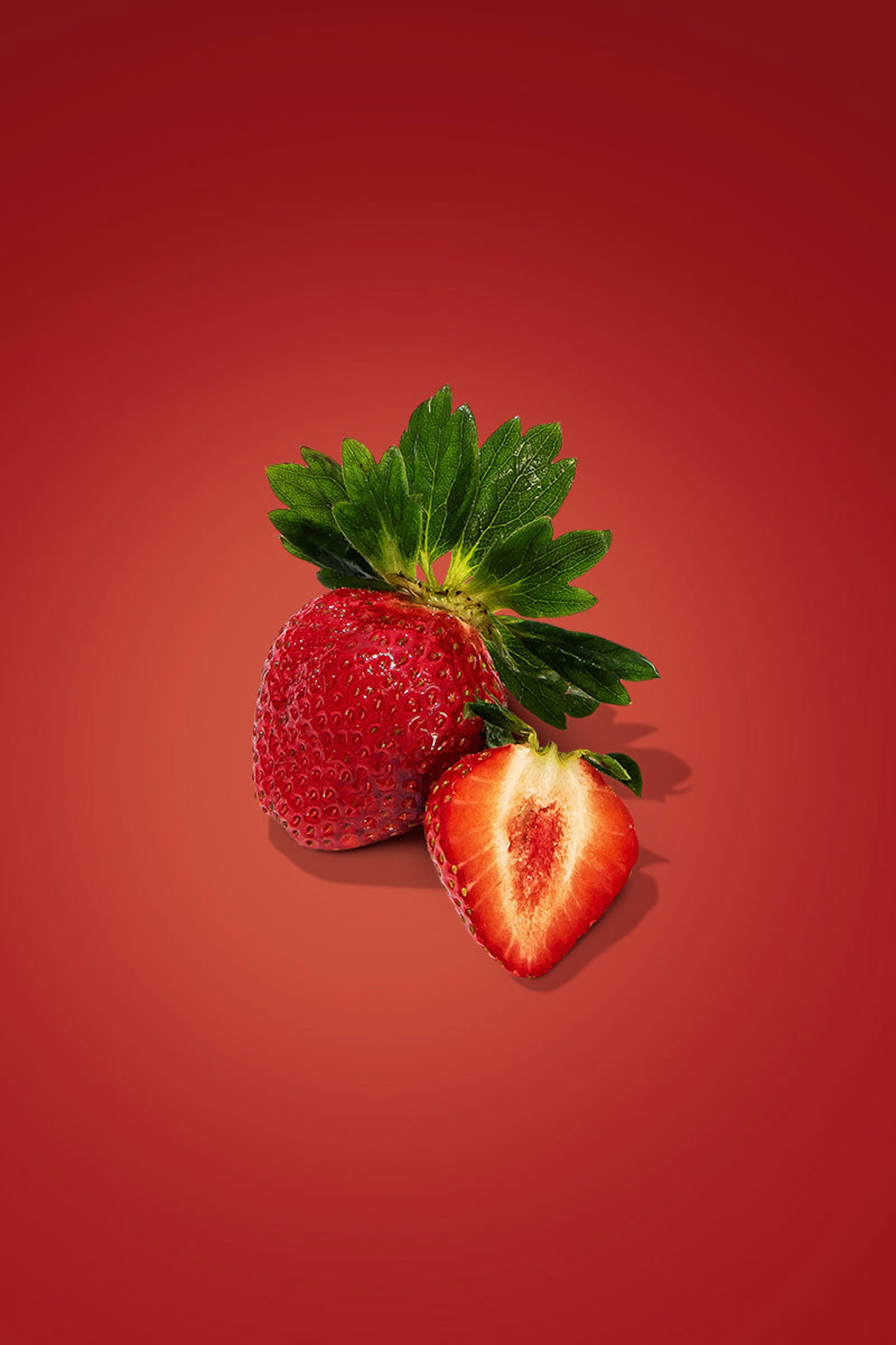 A whole strawberry next to a sliced strawberry half