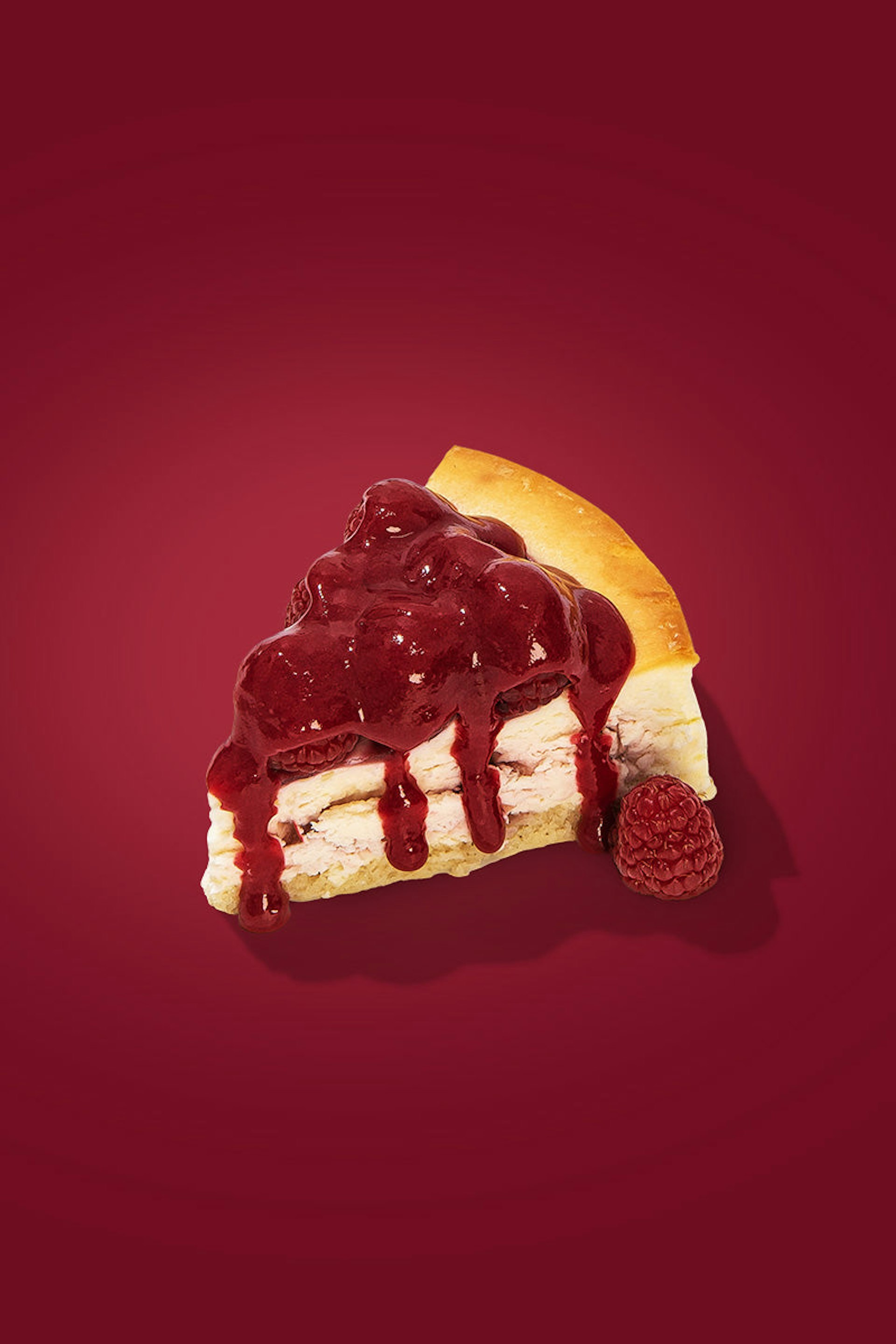 A slice of cheesecake drizzled with raspberry sauce and topped with more raspberries