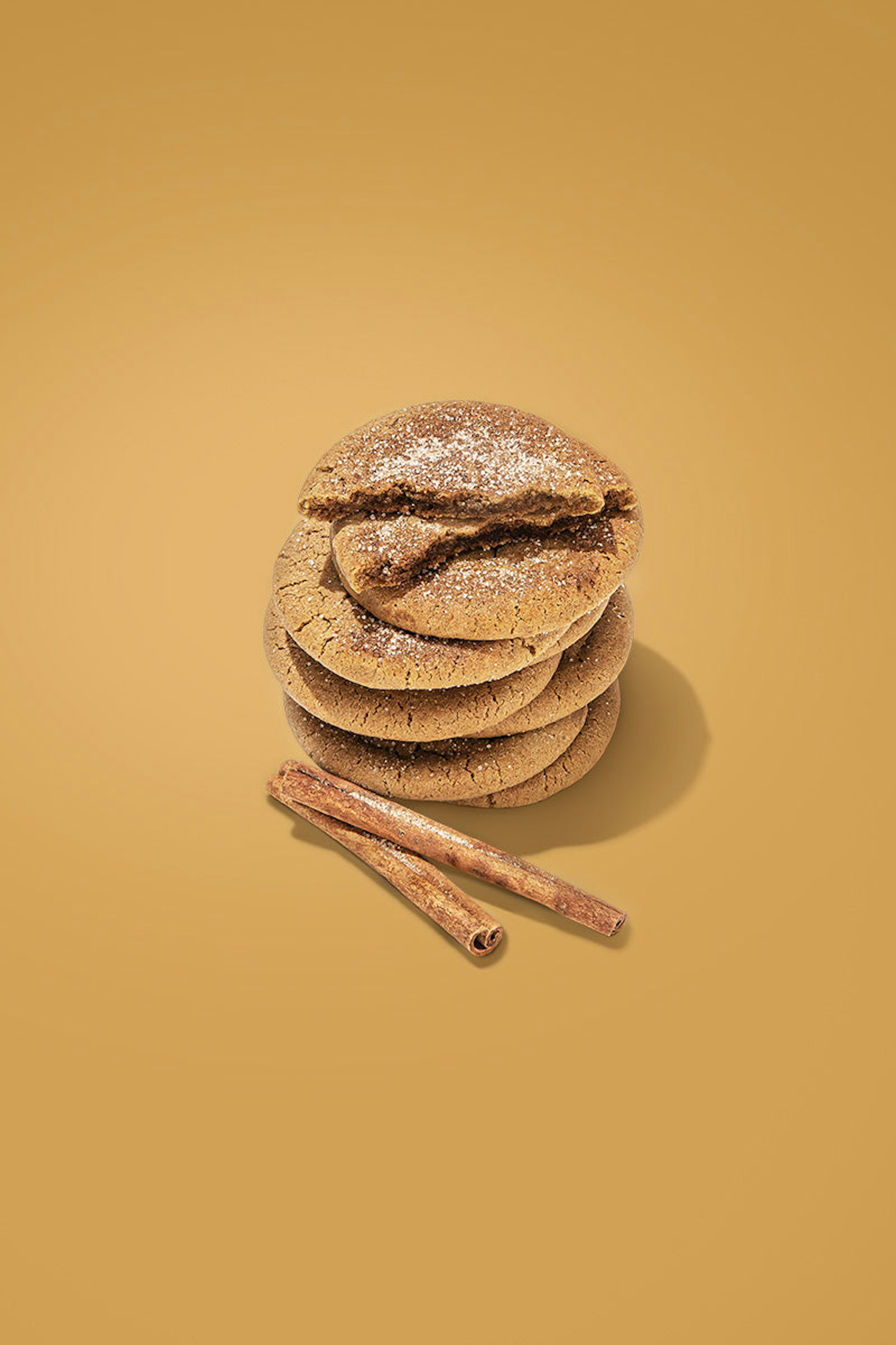 A pile of snickerdoodle cookies with two cinnamon sticks set to the side