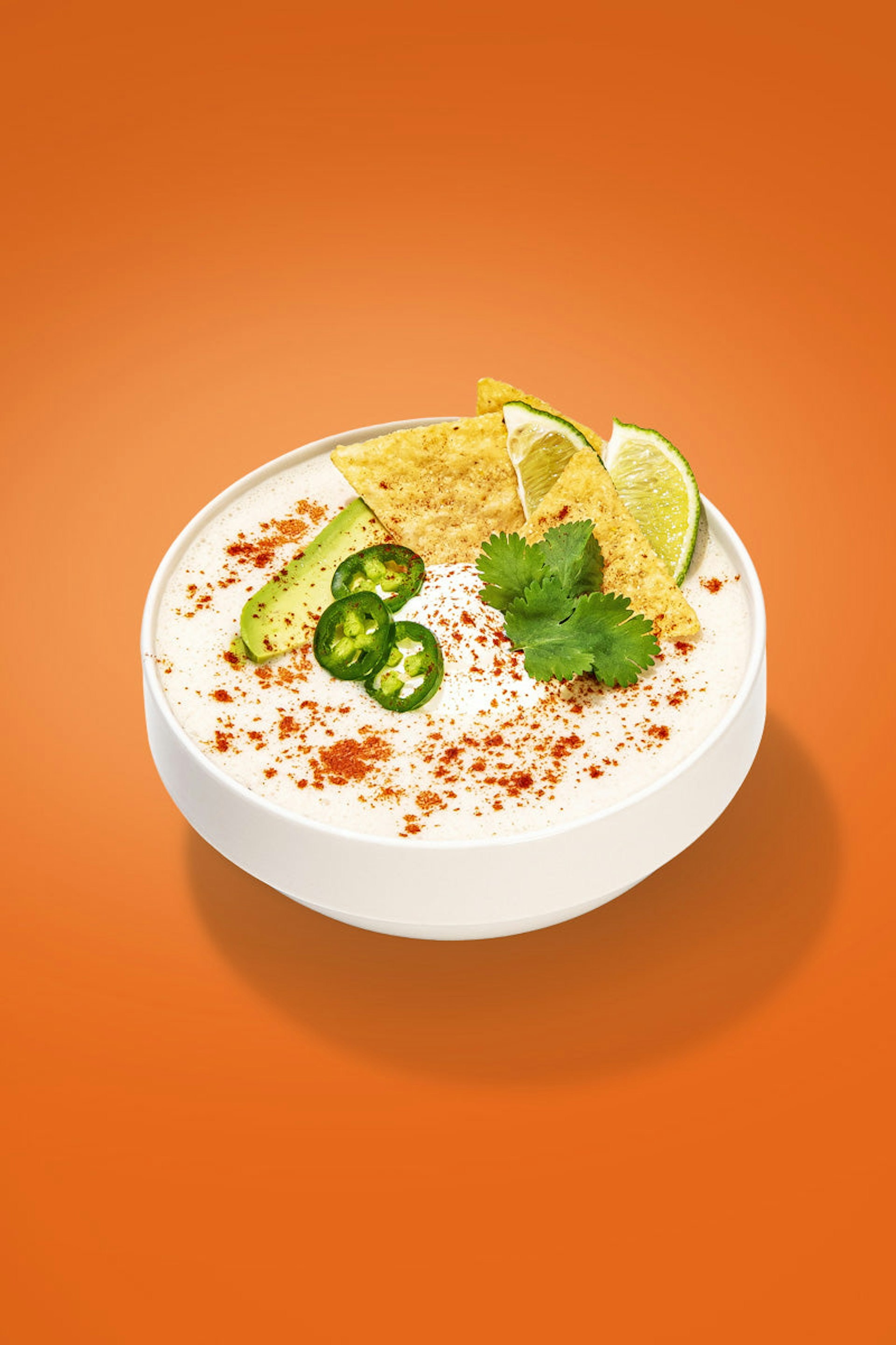 A bowl of creamy soup, spiced with chili powder and garnished with cilantro, lime, and tortilla chips.