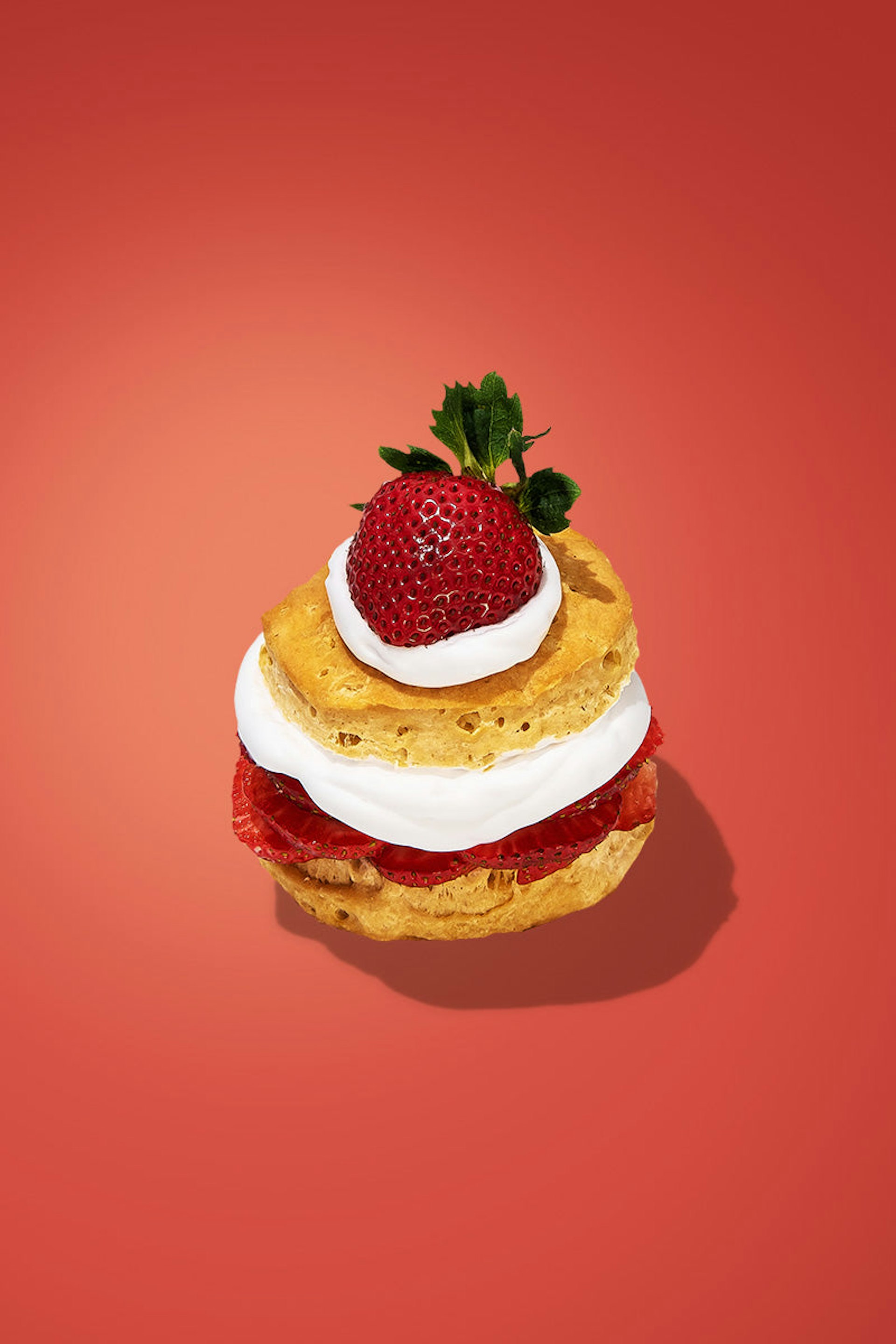 A mini strawberry shortcake. Whipped cream and a layer of sliced strawberries are sandwiched between slices of angel food cake, garnished with a whole strawberry on top.