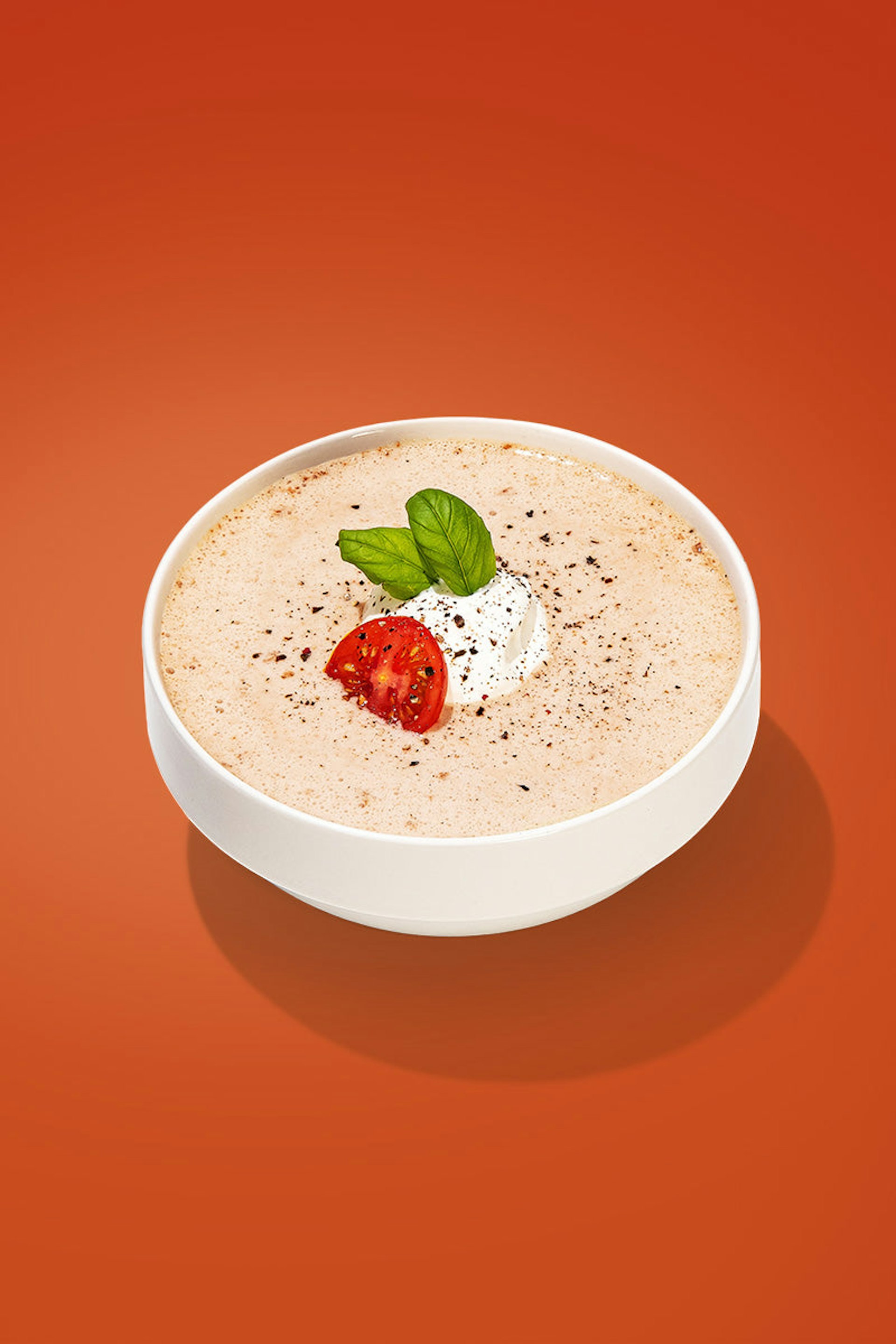 A bowl of creamy tomato soup, with basil and tomato garnishes