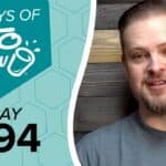 Promotional image featuring KETO CHOW branding. A teal graphic with a hexagonal pattern displays 100 DAYS OF KETO CHOW logo and text DAY 094. A man in a grey shirt smiles on the right against a dark wood background.