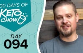 Promotional image featuring KETO CHOW branding. A teal graphic with a hexagonal pattern displays 100 DAYS OF KETO CHOW logo and text DAY 094. A man in a grey shirt smiles on the right against a dark wood background.