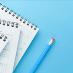 Three desk calendars with black spiral binding and white pages, displaying April and December dates, lie on a light blue background next to a blue pencil with a red eraser.