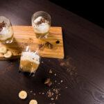 Three glasses of Banoffee Parfaits sitting on a cutting board, one glasslaying on its side