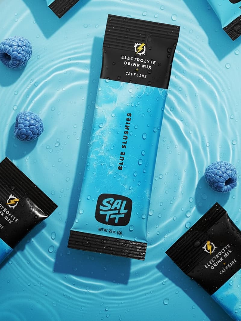 Blue electrolyte drink mix packet labeled Blue Slushies on rippling water surface, surrounded by fresh blueberries. Refreshing and vibrant.