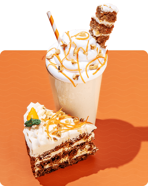 A slice of carrot cake next to a carrot cake keto chow shake garnished with carrot slices and a slice of carrot cake with an orange polka dot straw