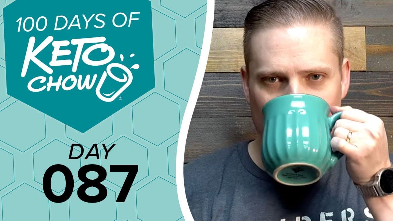 Digital banner featuring 100 DAYS OF KETO CHOW in white text with a cup and splash logo on a teal hexagon. Below it, DAY 087 is in black text on a light blue honeycomb pattern. A man drinks from a teal ribbed mug on the right against a wooden background.