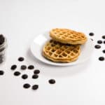 Two Chocolate Chip Chaffles on a white plate surrounded by chocolate chips.