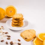 Stack of Orange Almond Shortbread cookies on a white plate, surrounded by sliced oranges and almonds.