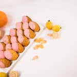 White tray withg pink icing topped madeleine cookies. Tray is surrounded by guava and grapefruit.
