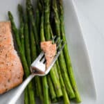 Close up-salmon and asparagus spears on a white plate and a fork with a piece of salmon.