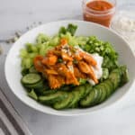 Close up of white bowl with sliced cucumbers, celery, green onions, and shredded buffalo chicken. A cup of cocktail sauce on the side