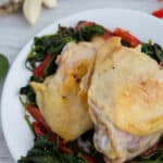 Two chicken thighs on a bed of cooked spinach and red peppers on a white plate.