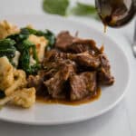 Close up- white plate with braised chuck roast with gravy, cauliflower and cooked spinach.