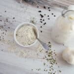 Top view - Ranch Dressing Mix in a small white bowl with a spoon. A bulb of garlic and bottle of ranch dressing sit to the side.