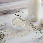 Side view - Ranch Dressing Mix in a small white bowl with a spoon. A bulb of garlic and bottle of ranch dressing sit to the side.