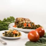 Close up - Two white plates with simmered collard greens, kale and red peppers. The larger plate also has a ham bone.