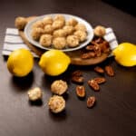 White plate filled with Lemon Cheesecake Bites. Surrounded by lemons and pecans.