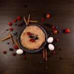 Top view - Sweet Cinnamon Egg White Protein Crepes, topped with berries. Eggs, cinnamon sticks and berries to the side.